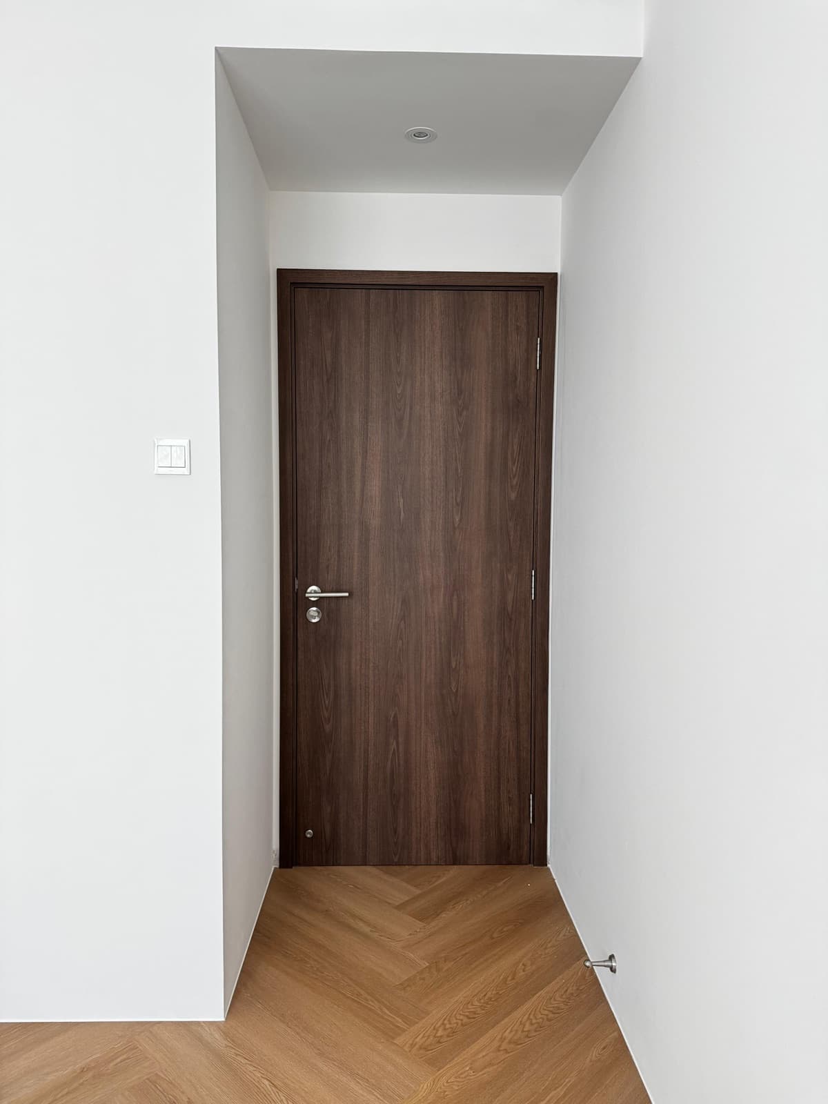 Bedroom door wrapped in dark wood-grain film above herringbone flooring