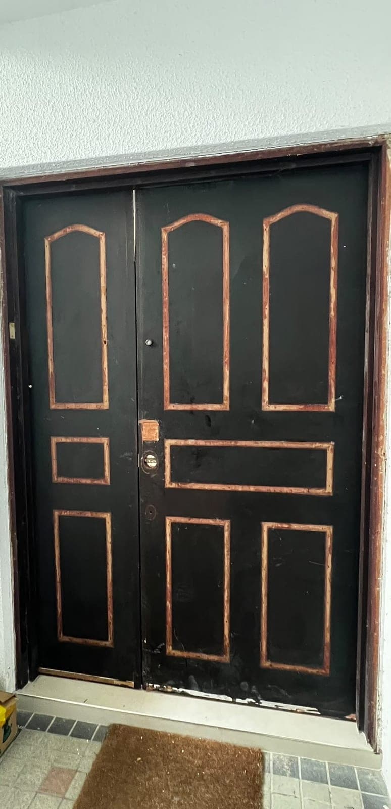 A black panelled double main door with worn trim in Loyang before wrapping