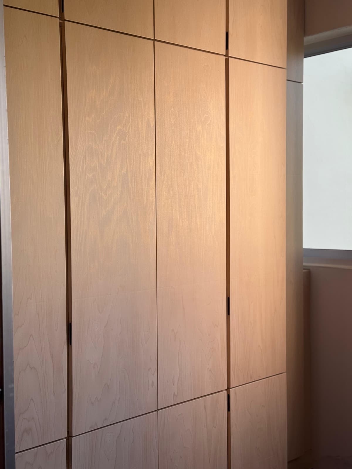 Full-height storage wall wrapped in light oak wood-grain